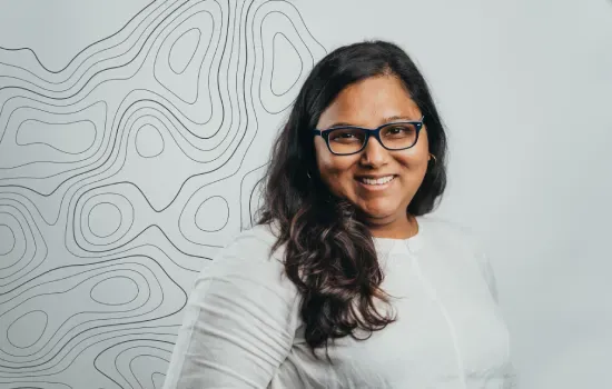 Davina Abel, Communication & Marketing Coordinator, smiling in glasses and a white blouse beside a contour-line wall