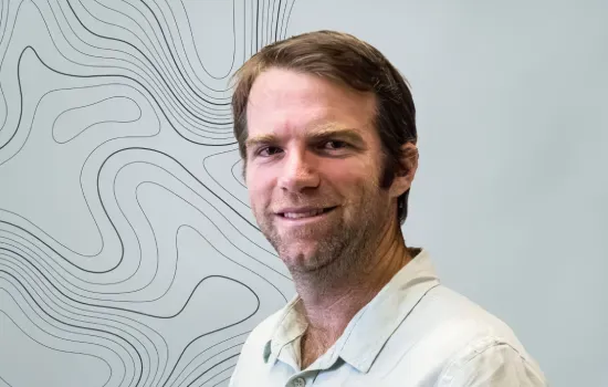 Portrait of Matthieu Vallet, Operations Manager at Novaterra, smiling in a light shirt beside a topographic line pattern