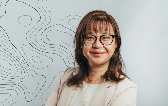 Stephanie Wong, Finance Manager at Novaterra, smiling in glasses and a beige blazer before a contour-line wall