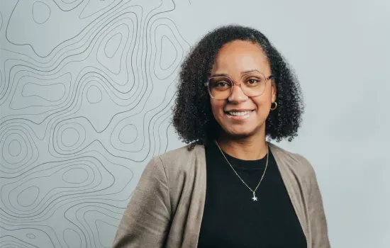 Karina Paul, Sales Executive at Novaterra, smiling in glasses and a beige blazer before a contour-line map wall