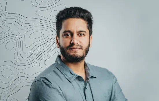Portrait of Tarun Dawoonauth, GIS Developer at Novaterra, in a grey shirt before a wall with topographic contour lines