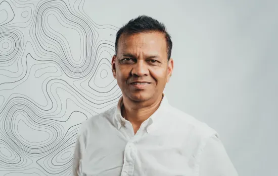 Portrait of Prithiviraj (Prit) Balloo, Head of Land Management, in a white shirt before a topographic contour pattern