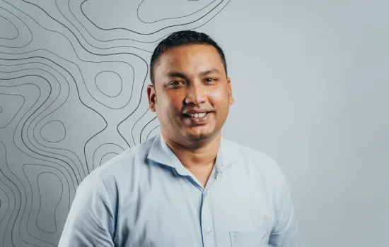 Jimmy Caullychurn, Novaterra messenger and office attendant, smiling in a light blue shirt against a contour-line wall