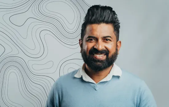 Portrait of Surendra Latchuman, Senior Permit & Regulatory Officer, smiling in a light blue sweater before a contour-line wall