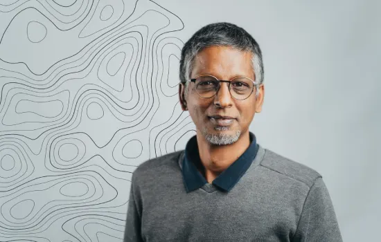 Govinda Naidoo, Manager - Land Surveying, in glasses and a grey sweater before a wall with topographic contour lines