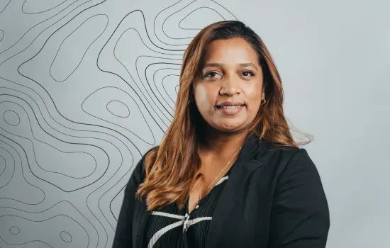Portrait of Virginie Malabar, HR Business Partner, in a black blazer against a grey topographic-pattern wall