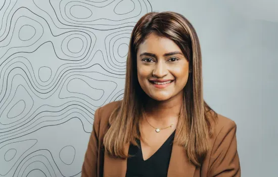Danushka Appadoo, Sales & Leasing Administration Manager at Novaterra, smiling in a brown blazer before a contour-line wall