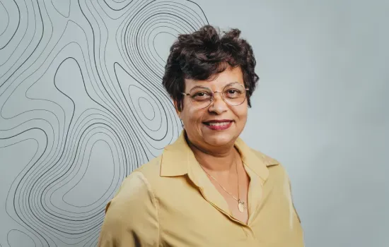 Portrait of Sabrina Mootoosawmy, Administrative Secretary, smiling in glasses and a mustard blouse before a contour-line wall