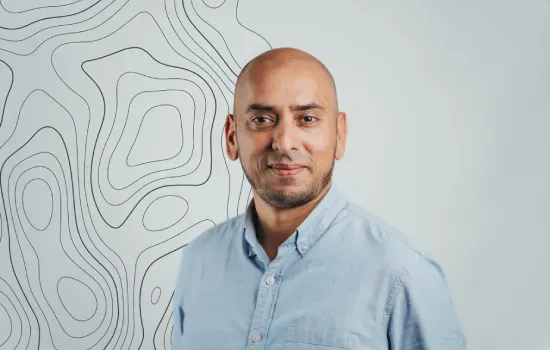 Portrait of Afzal Soobrattee, Novaterra architect, smiling in a light blue shirt before a topographic line wall