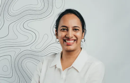 Portrait of Roochita Emamkhan, Novaterra accountant, smiling in a white shirt against a topographic line backdrop