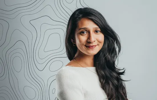 Vaneeda Chenchooliah, Communications Manager at Novaterra, smiling in a white top before a topographic line wall